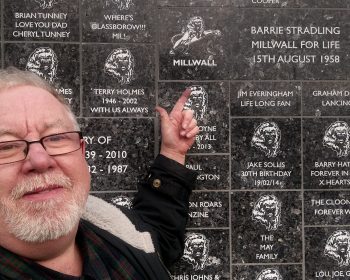 Barrie Stradling pointing at the Wall of Dedications at Millwall.