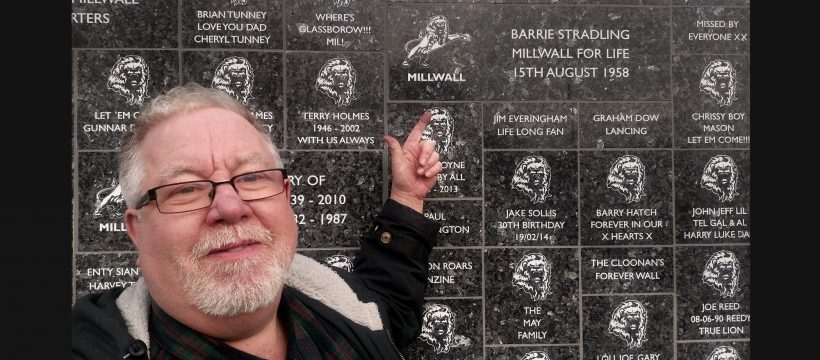Barrie Stradling pointing at the Wall of Dedications at Millwall.